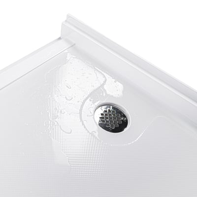 Gros plan de l'évacuation chromée sur un receveur de douche en acrylique blanc humide avec texture antidérapante pour cabines de douche accessibles en fauteuil roulant