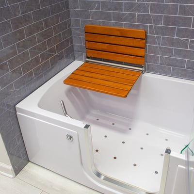 Folding teak wood shower seat mounted on the wall inside an Ella walk-in tub with air jets and low-step entry door
