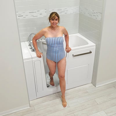 Woman in striped swimsuit stepping into the Ella Ultra Acrylic walk-in tub with open door and grab bar support