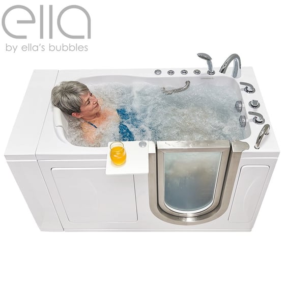 Mujer mayor relajándose en una bañera de acceso Ella Elite con chorros dobles de hidromasaje y una bebida en la bandeja lateral