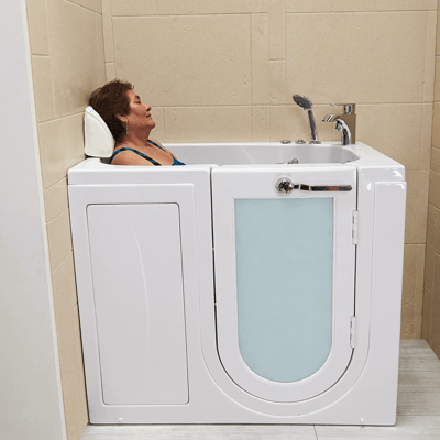 Mujer mayor descansando con los ojos cerrados en una almohada para la cabeza dentro de una bañera Ella con puerta de apertura interior esmerilada y ducha de mano