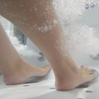 Close-up of bare feet on anti-slip walk-in tub floor surrounded by air bubble foot massage jets and foamy water