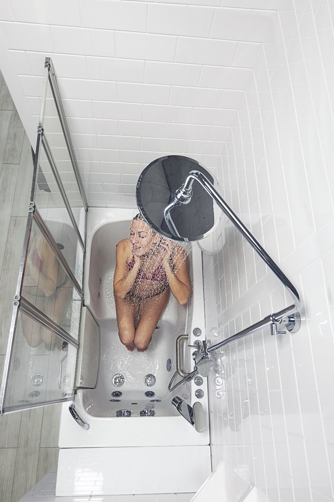 Une femme assise dans un combiné baignoire à porte et douche Ella Capri profitant de l’effet de pluie d’une colonne de douche de tête