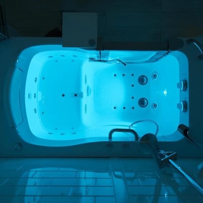 Vue de dessus de l’intérieur d’une baignoire à porte Ella illuminée d’un éclairage de chromothérapie bleu, mettant en valeur les jets et le sol antidérapant