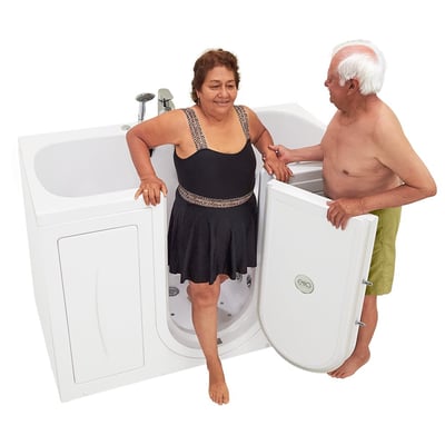 Senior woman stepping into the Ella Tub4Two two-seat walk-in bathtub as her partner holds the outward swing door open
