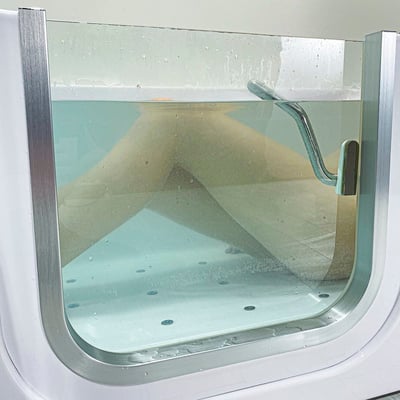 Gros plan sur la porte en acrylique transparent à ouverture vers l’intérieur d’une baignoire à porte allongée Ella remplie d’eau montrant les jets du fond antidérapant