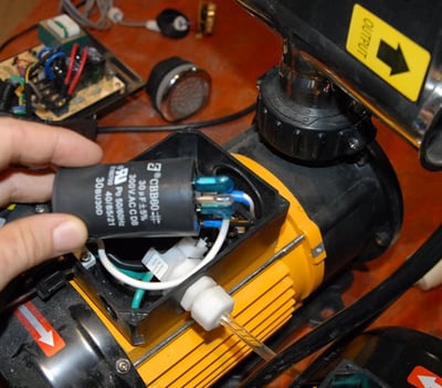 Main d’un technicien remplaçant un condensateur à l’intérieur du moteur de la pompe hydraulique d’une baignoire à porte Ella lors d’un service de réparation