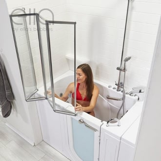 Woman in red swimsuit closing the glass folding shower screen door on an Ella walk-in bathtub with grab bars