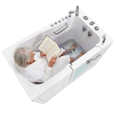 Senior woman reading while soaking in an Ella Monaco walk in tub as hydro foot massage jets bubble at her feet