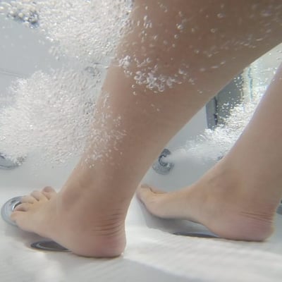 Underwater close-up of bare feet resting on anti-slip walk-in tub floor surrounded by therapeutic air bubble jets