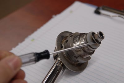 Technician using a screwdriver to disassemble a chrome lever door handle component on a lined notepad