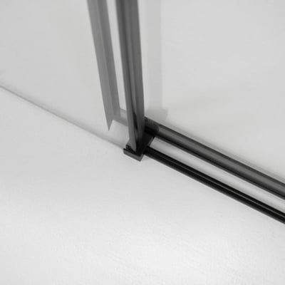 Primer plano del carril inferior en negro mate y la esquina del marco en la puerta de ducha corredera de vidrio templado Ella Primo