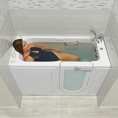 Femme se relaxant dans une baignoire à porte allongée Ella avec porte à ouverture vers l’extérieur, profitant du bain avec un verre de vin à proximité