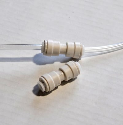 Deux raccords de tuyau d’air en plastique blanc à emboîtement, utilisés dans les systèmes de jets d’air des baignoires à porte, dont un est connecté à un tube transparent