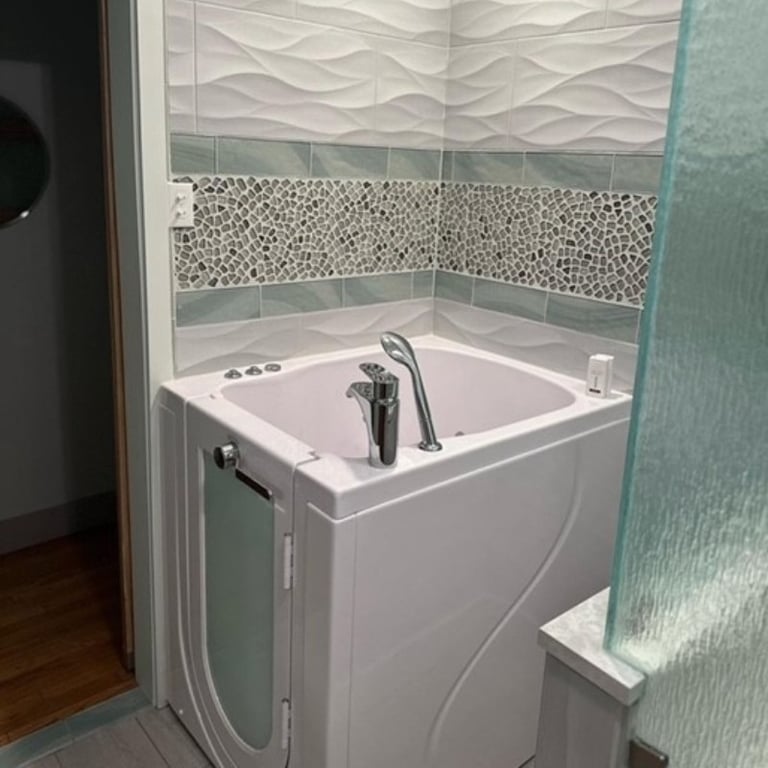 White Ella walk-in tub installed in a modern bathroom with pebble mosaic tile accent wall and glass panel divider