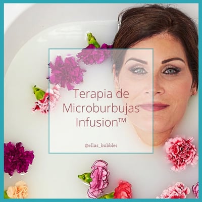 Mujer relajándose en una bañera con puerta con Ella's Bubbles Infusion terapia de microburbujas, rodeada de claveles flotantes en agua lechosa