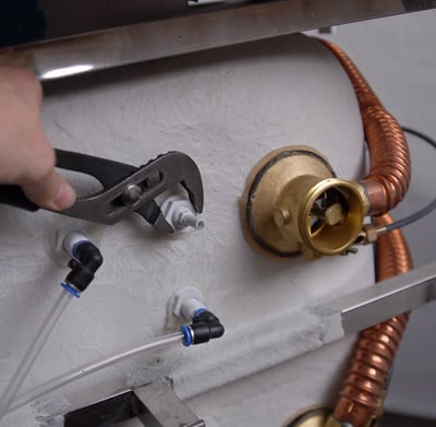Technicien utilisant une pince pour serrer les raccords de jet d’air et les composants de valve en laiton lors de l’assemblage d’une baignoire à porte