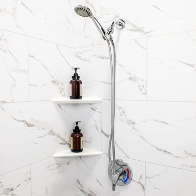 Close-up of chrome handheld shower head and hose with built-in corner shelves holding soap dispensers in a walk-in shower