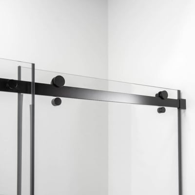 Primer plano de los herrajes y el carril de la puerta corredera en negro mate en un panel de mampara de ducha de vidrio templado transparente