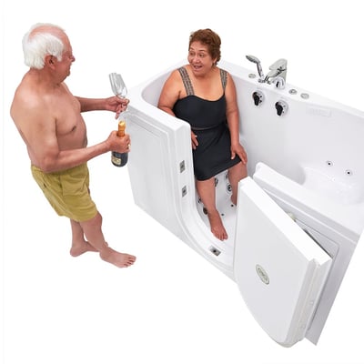 Senior couple celebrating together as woman sits inside an Ella walk-in tub with open door while man pours champagne