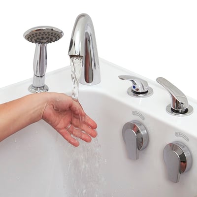 Hand testing water temperature flowing from chrome Roman faucet on an Ella walk-in tub with handheld showerhead and control knobs