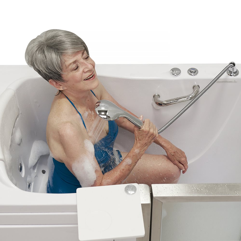 Femme âgée se rinçant avec la douchette, assise dans une baignoire à porte Ella Elite