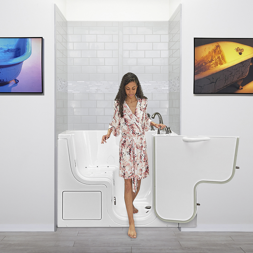 Woman in floral robe stepping into an Ella walk-in tub with open door, hydro jets, and white subway tile surround