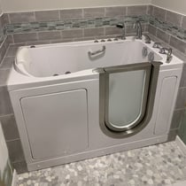 White Ella walk-in tub with outward swing door, hydrotherapy jets, and grab bar installed in tiled bathroom