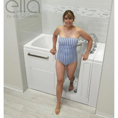 Woman in striped swimsuit stepping out through the open door of an Ella Ultra acrylic walk-in tub with grab bar