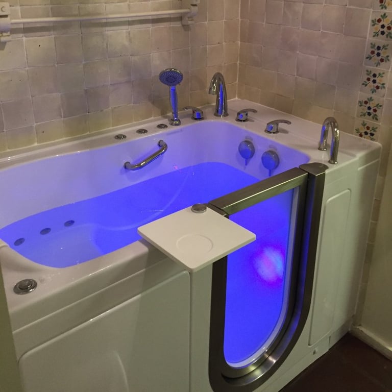 Ella walk-in tub with blue chromotherapy lighting, open door, swivel tray, jets, and chrome faucet set in tiled bathroom