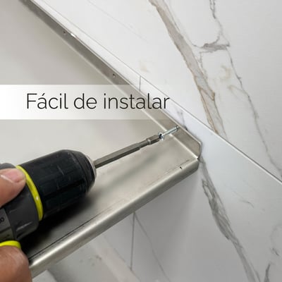 Instalador usando un taladro eléctrico para fijar un asiento de ducha de esquina de acero inoxidable a paneles de pared de mármol