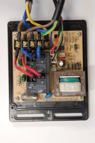 Close-up of an opened inline water heater control box showing circuit board, relays, transformer, and color-coded wiring connections