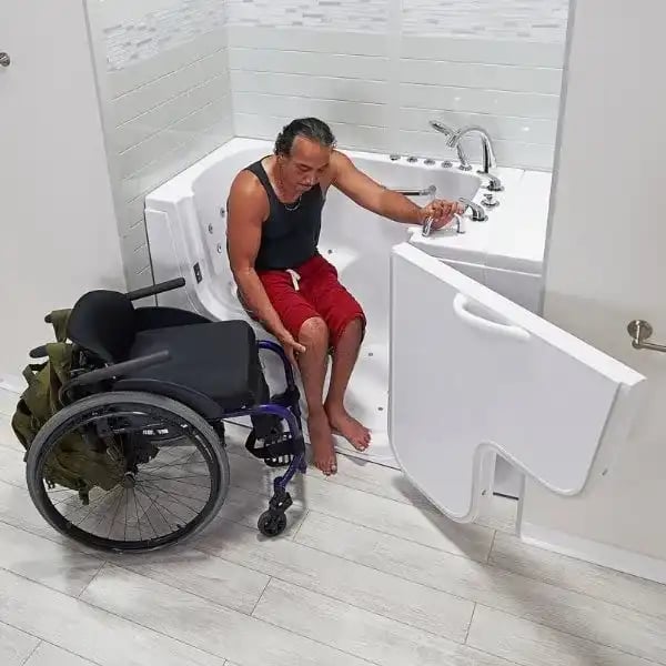 Man in wheelchair transferring into an Ella walk-in tub with wide outward-swing door designed for wheelchair accessibility