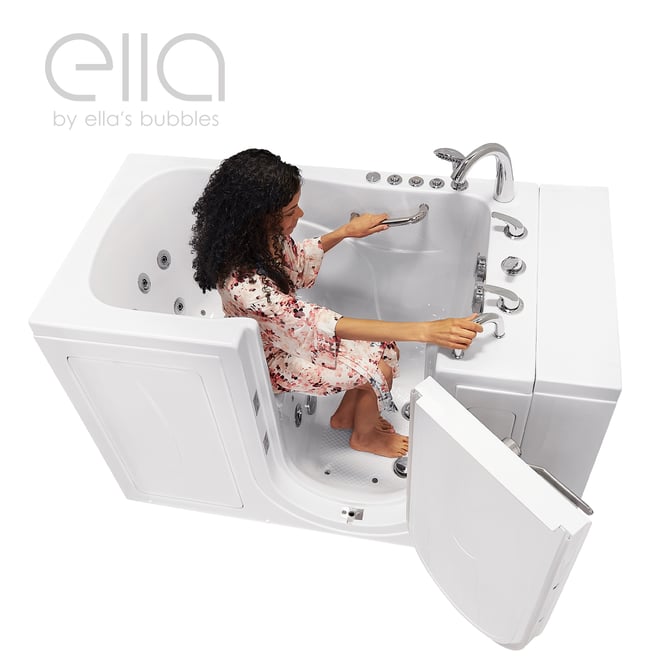 Woman in floral robe seated inside the Ella Capri walk-in tub gripping grab bars with open door and hydrotherapy jets visible
