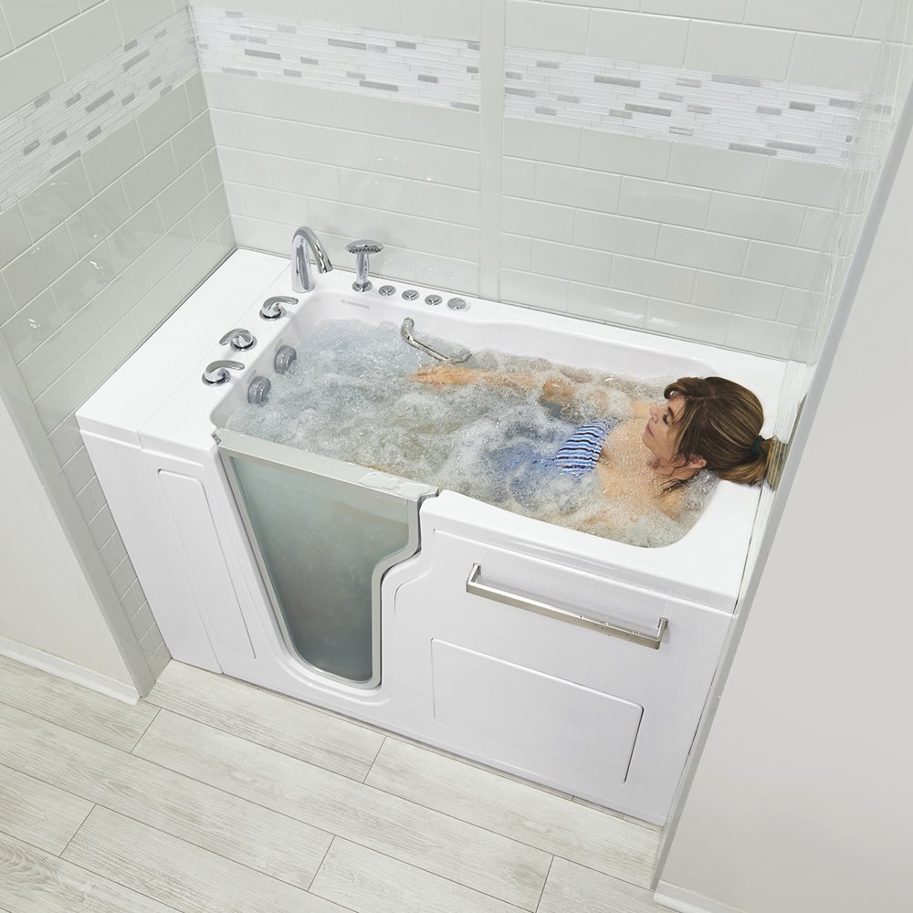 Femme se relaxant dans une baignoire à porte Ella Ultra en acrylique, avec des jets hydromassants qui bouillonnent autour d’elle, dans une salle de bains carrelée de blanc