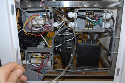 Main d’un technicien accédant au compartiment interne de la pompe et du câblage électrique d’une baignoire à porte Ella lors de l’installation