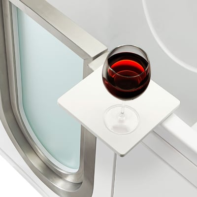 Gros plan d’un verre de vin rouge posé sur le plateau pivotant blanc de la baignoire à porte Ella Elite, à côté du cadre de porte en acier inoxydable