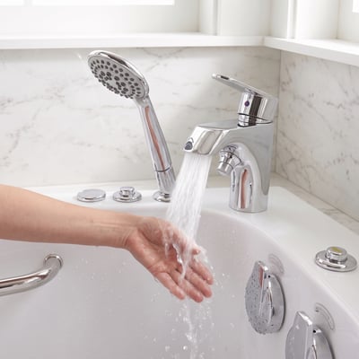 Chrome fast fill faucet and handheld shower wand on a walk-in tub deck, warm water running over a hand