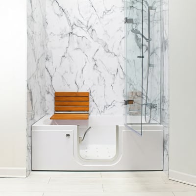 Ella walk-in tub with teak folding seat, open side door, and glass shower enclosure against marble vein walls