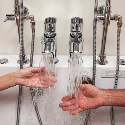 Two hands testing warm water flow from dual chrome faucets on the Ella Big4Two two-seat walk-in bathtub