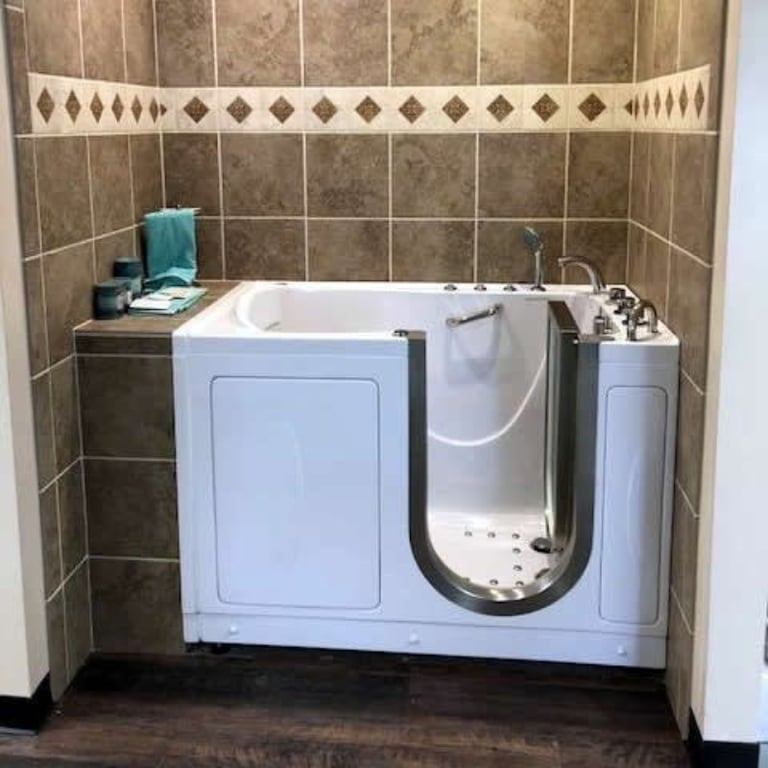 White Ella walk-in tub with open inward swing door installed in a tiled bathroom with decorative border and wood shelf