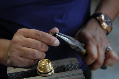 Technician using pliers to assemble a brass thermostatic control valve cartridge component during walk-in tub manufacturing
