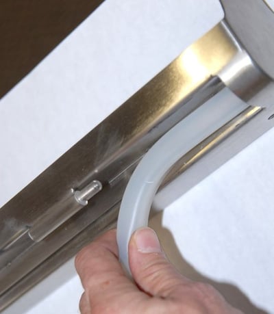 Close-up of a hand pressing a white rubber door seal into a stainless steel walk-in tub door frame track