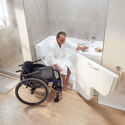 Man in a robe transferring from a wheelchair onto the seat of a wheelchair accessible walk-in tub