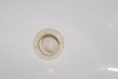 Gros plan d'un raccord de couvercle de retour rond beige monté à fleur sur la surface blanche d'une baignoire à porte