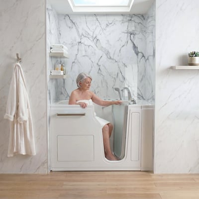 Senior woman wrapped in a towel seated inside the Ella Ultra walk-in tub with glass door and stainless steel accents in a marble bathroom