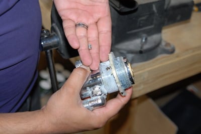 Technician holding a walk-in tub thermostatic control valve cartridge during inspection at a workshop workbench