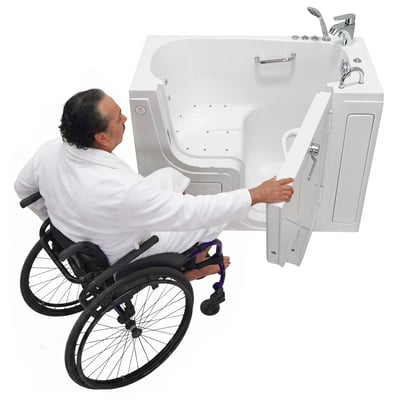 Man in a wheelchair reaching for the open outward door of a white wheelchair accessible walk-in tub
