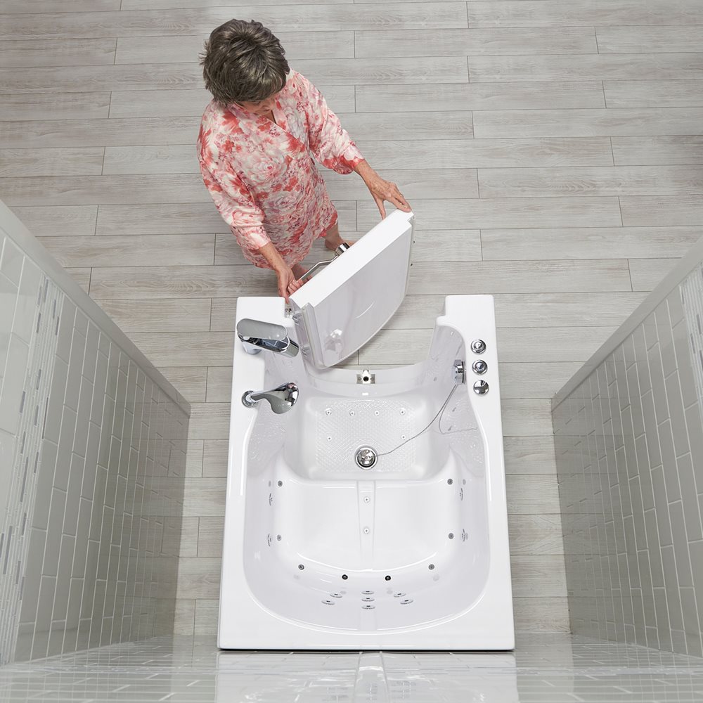 Senior woman opening the outward swing door of an Ella walk-in tub, aerial view showing the anti-slip floor and grab bar