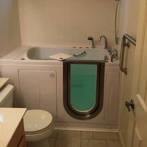 Ella walk-in tub with open inward-swing door, hydrotherapy jets, handheld shower, and stainless steel grab bar installed in small bathroom